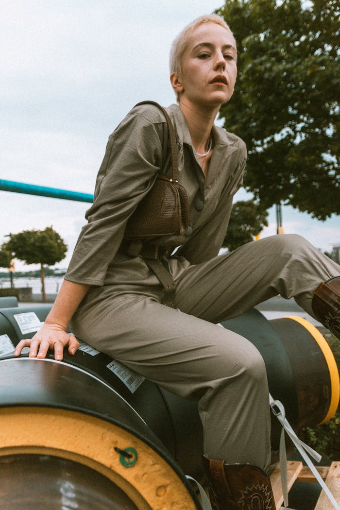 Stylish woman in a jumpsuit posing on industrial pipes in Berlin for a modern outdoor fashion shoot.
